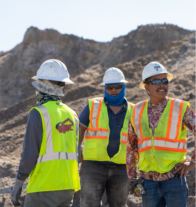 HBC, three employees standing in front of rocks, white hard hats, safety vests, hat under hard hat, blue head pull over, sunglasses, red and white print shirt, Rectangle-20.png, Culture